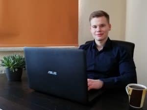 Junger Mann schaut in die Kamera, während er am Laptop sitzt